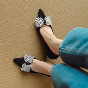Black high-heeled shoes with crystal embellishments worn by a person on a beige carpet.
