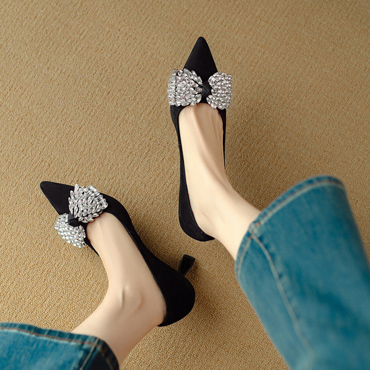 Black high-heeled shoes with decorative bows worn by a person on a beige background