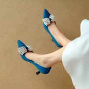 Blue high-heeled shoes with embellishments worn by a person on a beige background