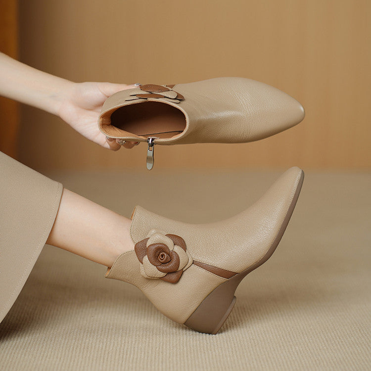 Beige ankle boots with floral design being worn on a neutral background