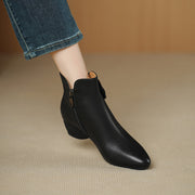 Black ankle boot worn with blue jeans on a beige surface