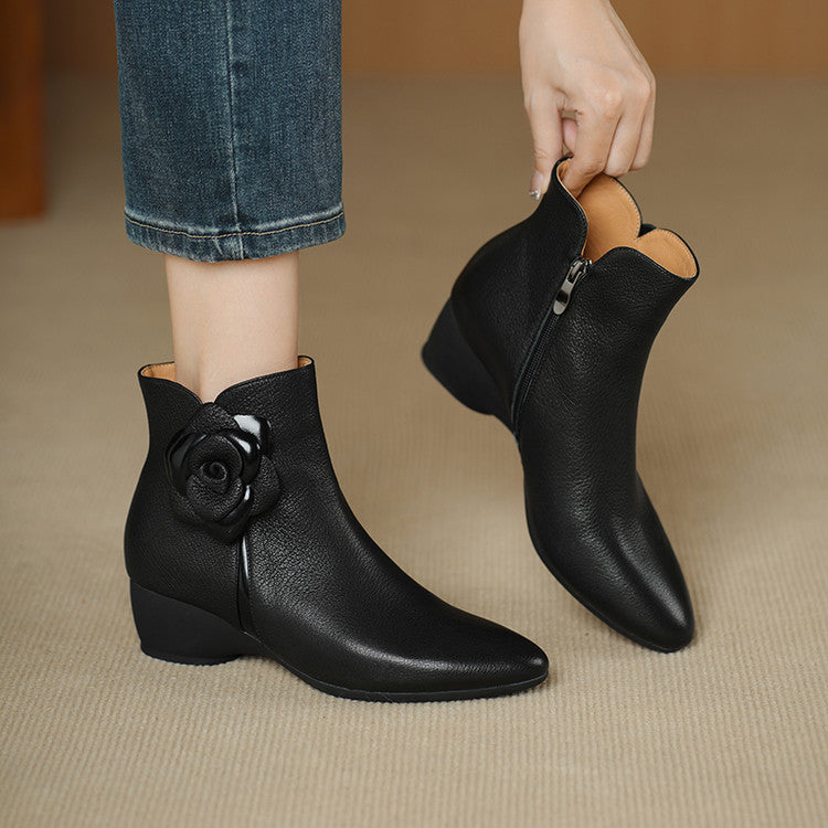 Black ankle boots with floral design worn by a person on a beige floor.