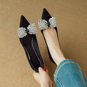 Black flats with large crystal bows held by a person wearing blue jeans.