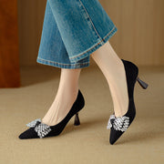 Black high-heeled shoes with decorative bows worn with blue jeans on a beige background