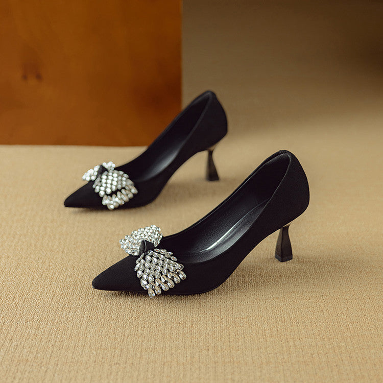 Black high-heeled shoes with decorative bows on a beige surface