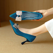 Blue high-heeled shoes with decorative bows held by a hand on a beige background