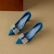 Pair of blue pointed-toe shoes with decorative embellishments on a beige surface