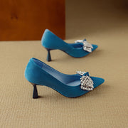 Blue high-heeled shoes with decorative bows on a beige surface