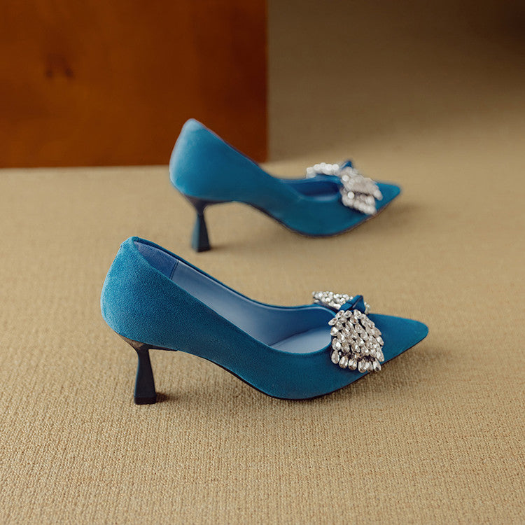 Blue high-heeled shoes with decorative bows on a beige surface
