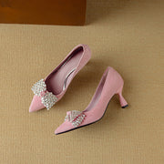 Pair of pink high-heeled shoes with decorative elements on a beige background