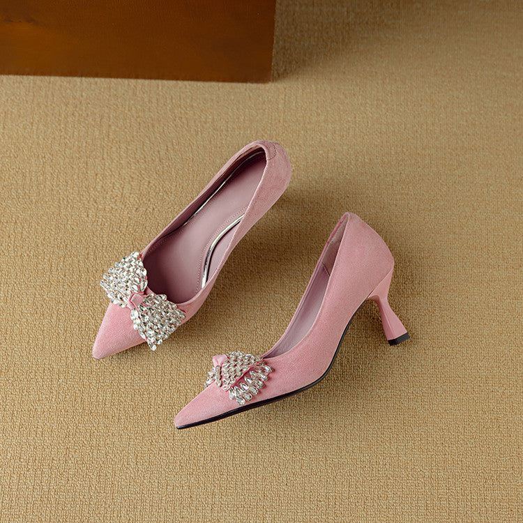 Pair of pink high-heeled shoes with decorative elements on a beige background