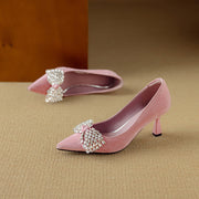 Pink high-heeled shoes with decorative bows on a beige surface