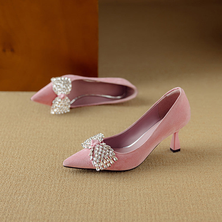 Pink high-heeled shoes with decorative bows on a beige surface