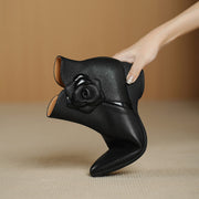 Black leather shoe with rose design held by a hand against a beige background