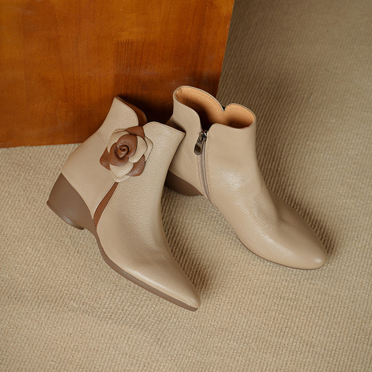 Pair of beige ankle boots with a decorative flower on a textured surface
