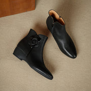 Pair of black leather ankle boots with a rose detail on a beige surface