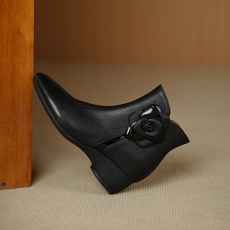 Black leather ankle boot with a rose detail on a beige surface.